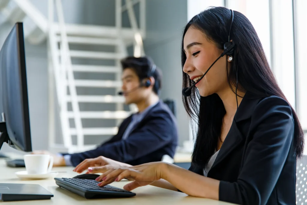 A smiling woman typing at a computer with a headset in a call center.